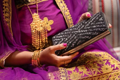 جزدان صغيرة بتصميم أنيق، منتجات ومساحيق التجميل، التقاليد في التقدم لطلب يد الفتاة، احتفالات سعيدة ومناسبات، صورة مقربة لسيدة عربية خليجية اماراتية تقوم باستعراض التحضيرات والتجهيزات للزفاف ترتدي الملابس التقليدية، إيماءات السعادة والفرح، الاحتفال بليلة العمر