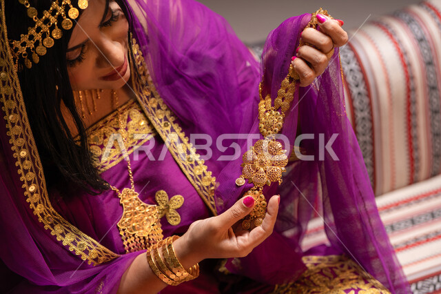 قطعة من الحلي عقد ذهبي، منتجات ومساحيق التجميل، التقاليد في التقدم لطلب يد الفتاة، احتفالات سعيدة ومناسبات، صورة مقربة لسيدة عربية خليجية اماراتية تقوم باستعراض التحضيرات والتجهيزات للزفاف ترتدي الملابس التقليدية، إيماءات السعادة والفرح، الاحتفال بليلة العمر