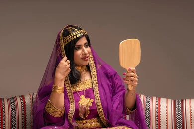 الاحتفالات والمناسبات السعيدة ، مفهوم التزيين والإطلالة المتألقة،التزين بالحلي و المجوهرات الذهبية ، استخدام مساحيق التجميل لإبراز الجمال، عروس عربية خليجية اماراتية ترتدي الزي التقليدي الشعبي تنظر لنفسها بالمرآة، الاستعداد للاحتفال بليلة العمر