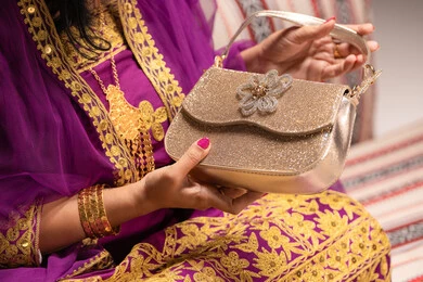 حقيبة باللون الذهبي والفضي للامع، مفهوم التزيين والإطلالة المتألقة، التزين بالحلي و المجوهرات الذهبية ، استخدام مساحيق التجميل لإبراز الجمال، عروس عربية خليجية اماراتية ترتدي الزي التقليدي الشعبي تقوم باستعراض التحضيرات والتجهيزات للزفاف، الاستعداد للاحتفال بليلة العمر