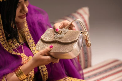 فتح الحقيبة باللون الذهبي، مفهوم التزيين والإطلالة المتألقة، التزين بالحلي و المجوهرات الذهبية ، استخدام مساحيق التجميل لإبراز الجمال، عروس عربية خليجية اماراتية ترتدي الزي التقليدي الشعبي تقوم باستعراض التحضيرات والتجهيزات للزفاف، الاستعداد للاحتفال بليلة العمر