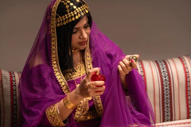 استخدام زجاجة عطر بالون الأحمر، مفهوم التزيين والإطلالة المتألقة، التزين بالحلي و المجوهرات الذهبية ، استخدام مساحيق التجميل لإبراز الجمال، عروس عربية خليجية اماراتية ترتدي الزي التقليدي الشعبي تقوم باستعراض التحضيرات والتجهيزات للزفاف، الاستعداد للاحتفال بليلة العمر