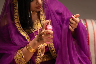 Spraying perfume from a pink bottle, the concept of decoration and a radiant appearance, adorning with jewelry and gold accessories, using cosmetics to highlight beauty, an Arab Gulf Emirati bride wearing traditional attire showcasing the preparations and arrangements for the wedding, getting ready to celebrate the night of a lifetime.