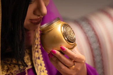 علبة من المسك الابيض، مفهوم التزيين والإطلالة المتألقة، التزين بالحلي و المجوهرات الذهبية ، استخدام مساحيق التجميل لإبراز الجمال، عروس عربية خليجية اماراتية ترتدي الزي التقليدي الشعبي تقوم باستعراض التحضيرات والتجهيزات للزفاف، الاستعداد للاحتفال بليلة العمر