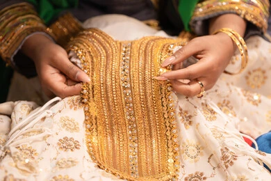 عرض تفاصيل ازياء المناسبات السعيدة ،التزين بالحلي و المجوهرات الذهبية ،الاحتفال بليلة العمر ، العادات و التقاليد الخليجية في الزواج ، صورة مقربة لعروس عربية خليجية اماراتية ترتدي الزي الشعبي التقليدي تقوم باستعراض التحضيرات والتجهيزات للزفاف