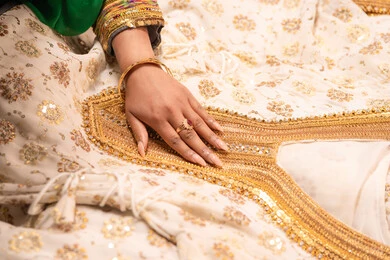 Show details of festive occasion attire, adornment with jewelry and gold ornaments, celebrating the night of a lifetime, Gulf customs and traditions in marriage, a close-up image of an Emirati Gulf Arab bride wearing traditional folk attire showcasing the preparations and arrangements for the wedding.