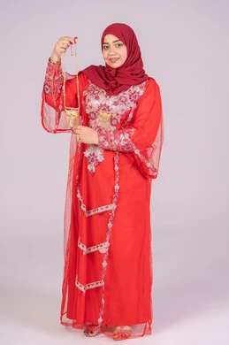 الحلي والمجوهرات الذهبية، احتفالات مناسبات وأفراح سعيدة، العناية بالأناقة والجمال، إيماءات السعادة والفرح، بورتريه لامرأة عربية خليجية اماراتية مبتسمة ترتدي الزي التقليدي الشعبي باللون الأحمر تقوم بعرض الحلي والمجوهرات الذهبية، صورة لكامل الجسم، خلفية بيضاء