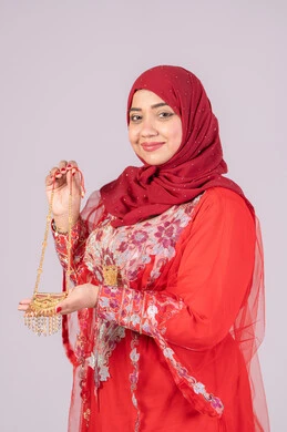 العناية والاهتمام بالأناقة والجمال، الحلي والمجوهرات الذهبية، احتفالات مناسبات وأفراح سعيدة، إيماءات السعادة والفرح، بورتريه لامرأة عربية خليجية اماراتية مبتسمة ترتدي الزي التقليدي الشعبي باللون الأحمر تقوم بعرض الحلي والمجوهرات الذهبية، خلفية بيضاء