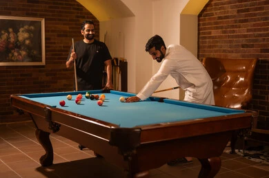 A group of young Arab Gulf Saudi men wearing casual and traditional clothing, playing billiards, a billiard table (snooker), youth activities and hobbies, a billiard café, professional players, competitions and challenges, fun and entertainment, a youth sports hall.