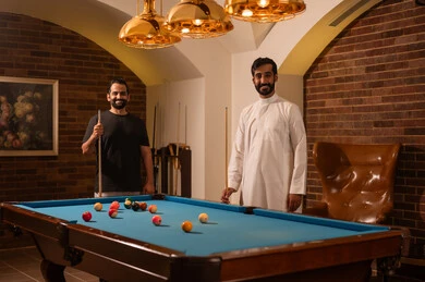 Expressions of joy for the camera, billiards café, youth activities and hobbies, billiards table (snooker), a group of young Arab Saudi Gulf men wearing casual and traditional attire, playing billiards, professional players, competitions and challenges, fun and entertainment, youth sports hall.