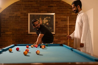 Fun and entertainment, competitions and challenges, professional players, dialogue and discussion among friends, billiard café, activities and youth hobbies, billiard table (snooker), a group of young Arab Saudi Gulf men wearing casual and traditional attire, playing billiards, youth sports hall.
