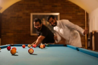 Entertainment and fun, professional players, dialogue and discussion among friends, billiard café, youth activities and hobbies, billiard table (snooker), a group of young Arab Saudi Gulf men wearing casual and traditional attire, playing billiards, youth sports hall.