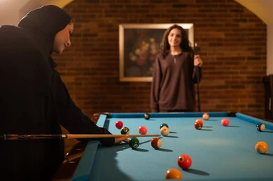 Youth activities and hobbies, playing among friends, professional players, dialogue and discussion among friends, billiard café, billiard table (snooker), a group of Arab Saudi Gulf women wearing abayas, one of them wearing a hijab, playing billiards, youth sports hall.