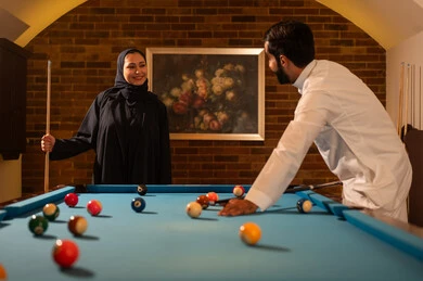 مفهوم العلاقات الزوجية الناجحة،  الاوقات المفضلة بين الازواج، أنشطه وهوايات شبابيه,  حوار ومناقشة بين الأصدقاء، مقهى البلياردو, طاولة بلياردو (السنوكر), رجل وزوجته عرب سعوديون خليجيون يرتدي يرتدي الزي التقليدي, يلعبون لعبة البلياردو، صاله رياضيه شبابيه