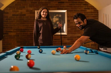 Strengthening the relationship between partners, successful marital relationships, favorite times between spouses, dialogue and discussion among friends, billiard café, billiard table (snooker), a man and his wife, Arab Saudi Gulf nationals, dressed in casual attire playing billiards, a youth sports hall.