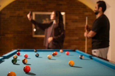Documenting beautiful moments through selfies, successful marital relationships, favorite times between couples, dialogue and discussion among friends, billiard café, billiard table (snooker), a man and his wife, Arab Saudis from the Gulf, dressed in casual attire playing billiards.