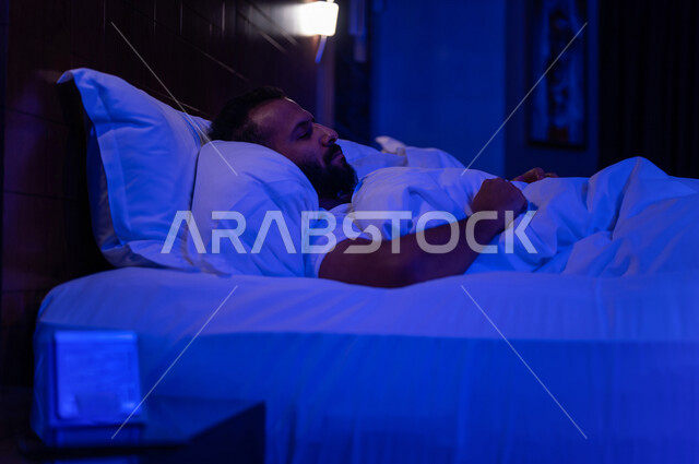 رجل عربي خليجي سعودي ينام في سرير منعش ومريح على وسادة بيضاء ناعمة، الاسترخاء والاستمتاع بنوم هاديء وصحي