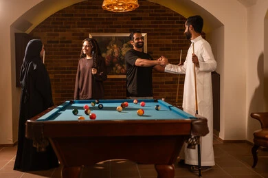 Farewell and goodbye to friends, a group of Arab Saudi Gulf friends wearing casual clothes and traditional attire, playing billiards, billiard hall, billiard table (snooker), youth activities and hobbies, billiard café, professional players, competitions and challenges, fun and entertainment.