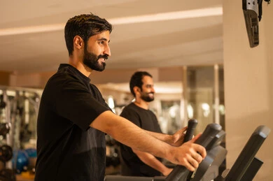 الالتقاء مع الاصدقاء في النادي، نشاط شبابي يساعد على المرونة البدنية,  أهمية الرياضة لبناء جسد قوي، الاهتمام بالصحة واللياقة الجسدية، رجل سعودي يمارس تمرين لتحسين وضعية الجسم والتوازن، شاب عربي خليجي سعودي يرتدي الزي الرياضي يقوم بممارسة التمارين على جهاز المشي