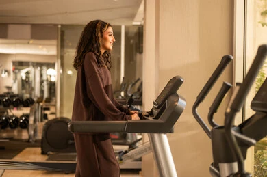 أسلوب حياة صحية، استخدام الأجهزة التقنية الحديثة، مفهوم حرق الدهون و إنقاص الوزن، صورة لفتاة عربية خليجية سعودية ترتدي الملابس الرياضية تضع على رأسها سماعة الهيدفون، الاستماع للموسيقى أثناء ممارسة التمارين الرياضية على جهاز المشي