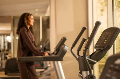A fun time while exercising on the treadmill, a healthy lifestyle, using modern technological devices, the concept of burning fat and losing weight, a picture of a Saudi Gulf Arab girl wearing sportswear, listening to music while working out on the treadmill.
