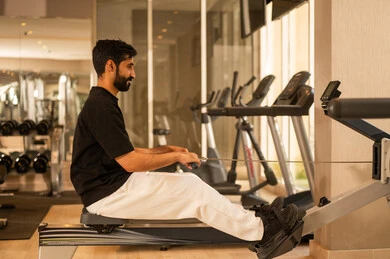 Health and physical fitness, the importance of sports in building a strong body, a youthful activity that helps with physical flexibility, a Saudi man practicing an exercise to improve body posture and balance, a young Arab Gulf Saudi wearing sportswear exercising on a rowing machine, using sports equipment.