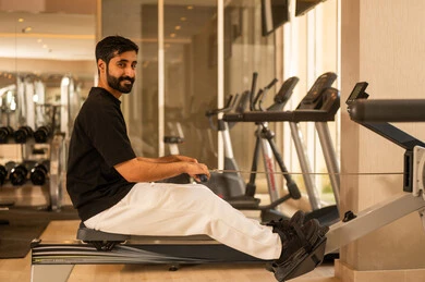 Attention to health and physical fitness, the importance of sports in building a strong body, a youthful activity that helps with physical flexibility, a Saudi man practicing an exercise to improve body posture and balance, a young Arab Gulf Saudi man wearing sportswear exercising on a rowing machine, using sports equipment.