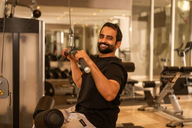 رجل سعودي يمارس أنشطة لتقوية العضلات، استخدام الأجهزة الرياضية، الاهتمام بالصحة واللياقة الجسدية، إيماءات القوة والثقة، رياضة كمال الأجسام، أسلوب حياة صحي، شاب عربي خليجي سعودي يرتدي الزي الرياضي يقوم بممارسة تمارين رفع الأوزان