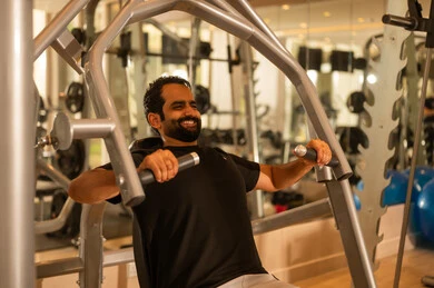 إيماءات القوة والثقة، رياضة كمال الأجسام، أسلوب حياة صحي، الاهتمام بالصحة واللياقة الجسدية، استخدام الأجهزة الرياضية، شاب عربي خليجي سعودي يرتدي الزي الرياضي يقوم بممارسة تمارين رفع الأوزان، رجل سعودي يمارس أنشطة لتقوية العضلات