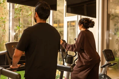 Concern for health and physical fitness, enduring tough workouts to maintain fitness, having fun during exercise, a healthy lifestyle, using modern technological devices, the concept of burning fat and losing weight, a picture from behind of an Arab Gulf couple from Saudi Arabia wearing sportswear.