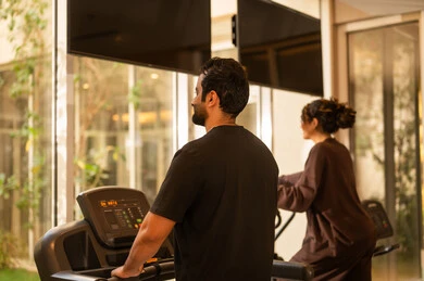 Body sculpting and muscle strengthening, enduring tough workouts to maintain fitness, having fun during exercise, a healthy lifestyle, using modern technological devices, the concept of burning fat and losing weight, a picture from behind of an Arab Gulf couple from Saudi Arabia wearing sportswear.