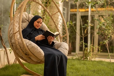 قضاء وقت الفراغ في مطالعة الكتب والروايات، شابة عربية خليجية سعودية ترتدي عباءة تجلس على الارجوحة تقوم بقراءة كتاب، قضاء وقت ممتع في الهواء الطلق في احدى الشاليهات السياحية