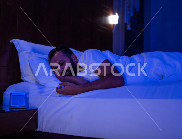 رجل عربي خليجي سعودي ينام في سرير منعش ومريح على وسادة بيضاء ناعمة، الاسترخاء والاستمتاع بنوم هاديء وصحي
