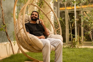 استخدام جهاز تقني حديث، شاب عربي خليجي سعودي يرتدي الزي الكاجوال يجري مكالمة هاتفية عبر الهاتف المحمول يجلس في الهواء الطلق، الجلسة الخارجية في احدى الشاليهات، الرد على الاتصال الهاتفي بتعابير السرور