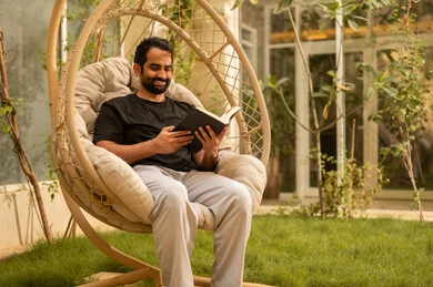Spending enjoyable time with oneself by reading stories and novels, the concept of self-learning and self-cultivation, an Arab Gulf Saudi man dressed in casual attire sitting outdoors reading a book, developing vocabulary.