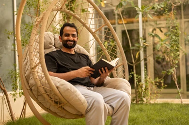 Spending enjoyable time with oneself by reading stories and novels, the concept of self-learning and self-cultivation, an Arab Gulf Saudi man dressed in casual attire sitting outdoors reading a book, developing vocabulary.
