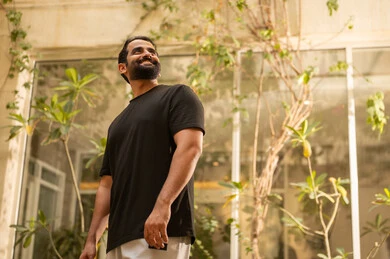 Gestures of happiness and joy, solitude with oneself in quiet places to calm the nerves, a young Arab Gulf Saudi man wearing casual attire in the garden, enjoying time outdoors in one of the tourist chalets in the Kingdom of Saudi Arabia.