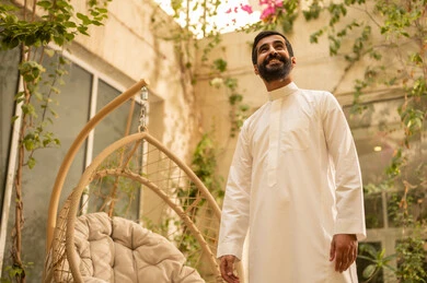 ايماءات السعادة والسرور، الخلوة مع النفس في الاماكن الهادئة لتهدئة الاعصاب، شاب عربي خليجي سعودي يرتدي الزي التقليدي في الحديقة، قضاء وقت ممتع في الهواء الطلق في احدى الشاليهات السياحية في المملكة العربية السعودية