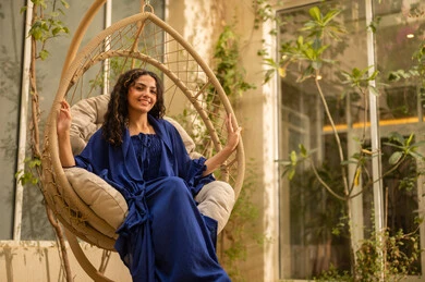 الخلوة مع النفس في الاماكن الهادئة لتهدئة الاعصاب، ايماءات السعادة والسرور، شابة عربية خليجية سعودية ترتدي عباءة تجلس على الارجوحة في الحديقة، قضاء وقت ممتع في الهواء الطلق في احدى الشاليهات السياحية في المملكة العربية السعودية