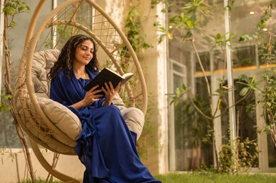 قضاء وقت الفراغ في مطالعة الكتب والروايات، شابة عربية خليجية سعودية ترتدي عباءة تجلس على الارجوحة تقوم بقراءة كتاب، قضاء وقت ممتع في الهواء الطلق في احدى الشاليهات السياحية