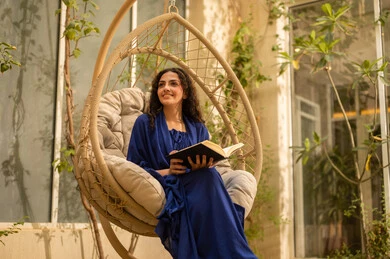 Spending free time reading books and novels, a young Arab Gulf Saudi woman wearing an abaya sits on a swing reading a book, enjoying time outdoors in one of the tourist chalets.