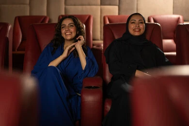 تعابير الاندماج والتفاعل ، متابعة الفيلم المفضل، الاستمتاع بمشاهدة الأفلام داخل السينما، امرأة عربية خليجية سعودية محجبة ترتدي عباءه مع صديقتها ، التسلية والترفيه بقضاء أوقات ممتعة