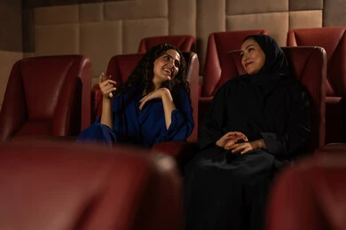 متابعة الفيلم المفضل، الاستمتاع بمشاهدة الأفلام داخل السينما،تعابير الاندماج والتفاعل ،  امرأة عربية خليجية سعودية محجبة ترتدي عباءه مع صديقتها ، التسلية والترفيه بقضاء أوقات ممتعة