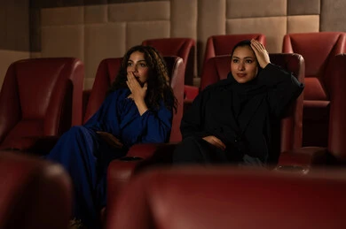 Expressions of integration and interaction, following the favorite movie, enjoying watching movies in the cinema, a Saudi Arabian Gulf woman wearing a hijab and an abaya with her friend, fun and entertainment by spending enjoyable times.