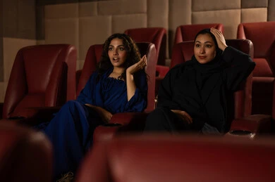 Expressions of integration and interaction, following the favorite movie, enjoying watching movies in the cinema, a Saudi Arabian Gulf woman wearing a hijab and an abaya with her friend, fun and entertainment by spending enjoyable times.