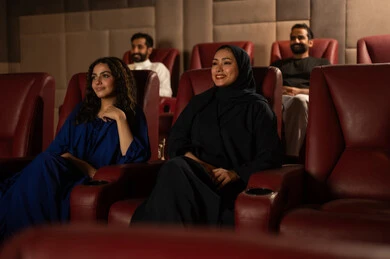 الاستمتاع بمشاهدة الأفلام داخل السينما،متابعة الفيلم المفضل، ،تعابير الاندماج والتفاعل ،  امرأة عربية خليجية سعودية محجبة ترتدي عباءه مع صديقتها ، التسلية والترفيه بقضاء أوقات ممتعة