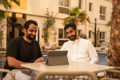 Watching movies and series on a mobile tablet, gestures of happiness and enjoyment, outdoor youth activities, spending enjoyable and entertaining time with friends, two Arab Gulf friends from Saudi Arabia sitting in one of the chalets.