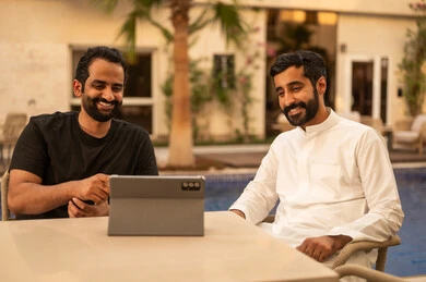 Watching movies and series on a mobile tablet, gestures of happiness and enjoyment, outdoor youth activities, spending enjoyable and entertaining time with friends, two Arab Gulf friends from Saudi Arabia sitting in one of the chalets.