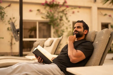 Entertainment and leisure, spending enjoyable time reading in one of the chalets, the concept of cleanliness and caring for the home garden, an Arab Gulf Saudi man wearing casual attire, recreational tourist places.