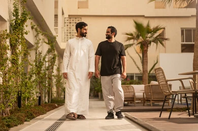 Youth activities outdoors, having a fun and entertaining time with friends, two Arab Gulf friends from Saudi Arabia strolling and walking in the park, gestures of happiness and enjoyment.